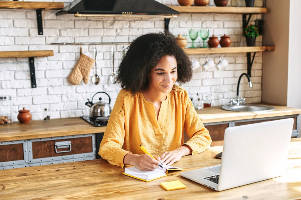 Schönes Afro-Mädchen schreibt vom Laptop aus in ein Notizbuch